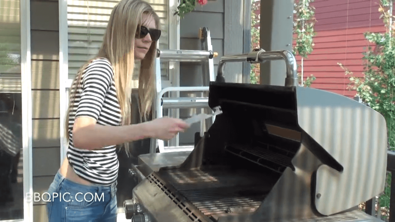 Photo of woman holding the BBQ Pic in front of a dirty BBQ, she's showing how to use the BBQ Pic. 